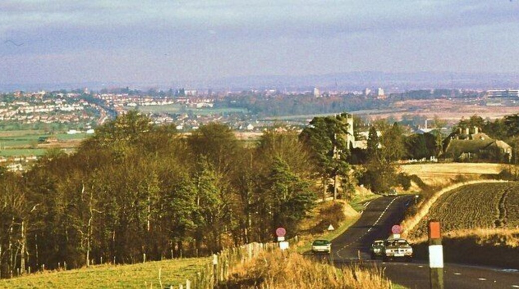 The A361 above Wroughton These days the road is numbered as A4361, for reasons better known to the highway authorities. The view down the hill includes the junction with the minor road to Elcombe, the tower of Wroughton parish church and the buildings of Swindon in the distance.