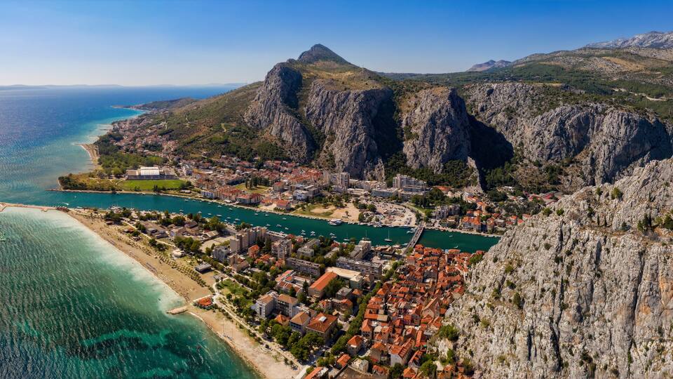 A coastal town with a mountain backdrop, clear blue sea, and a winding road.
