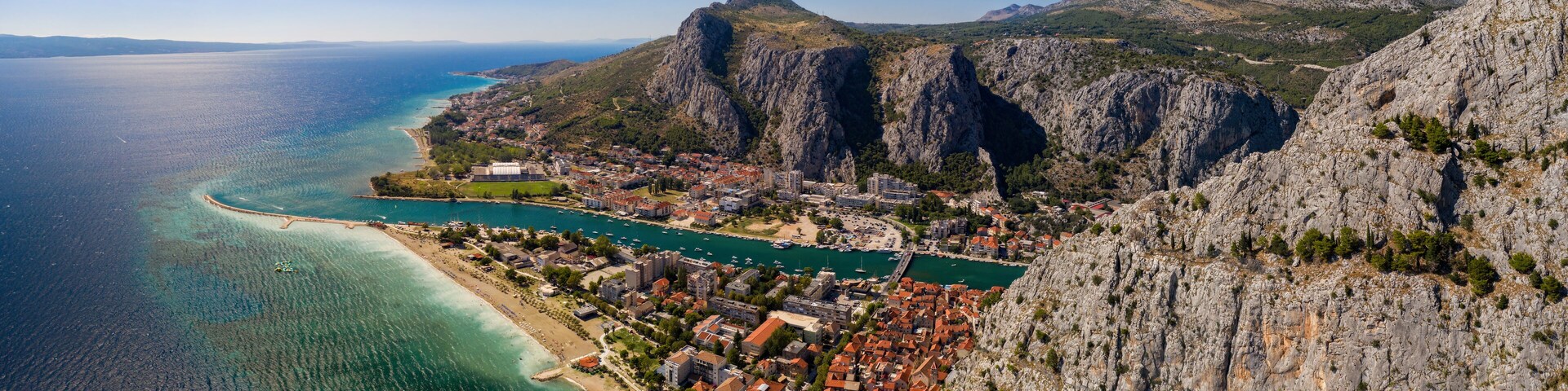 A coastal town with a mountain backdrop, clear blue sea, and a winding road.