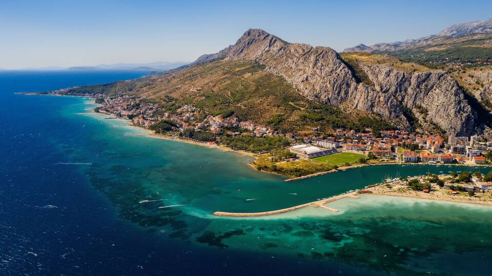 A coastal town with a mountain backdrop, clear turquoise waters, and a prominent rocky peak.