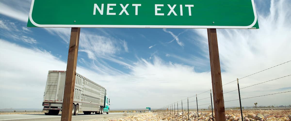 Señal verde de salida de autopista para California City, con cielo despejado y un camión en la carretera.