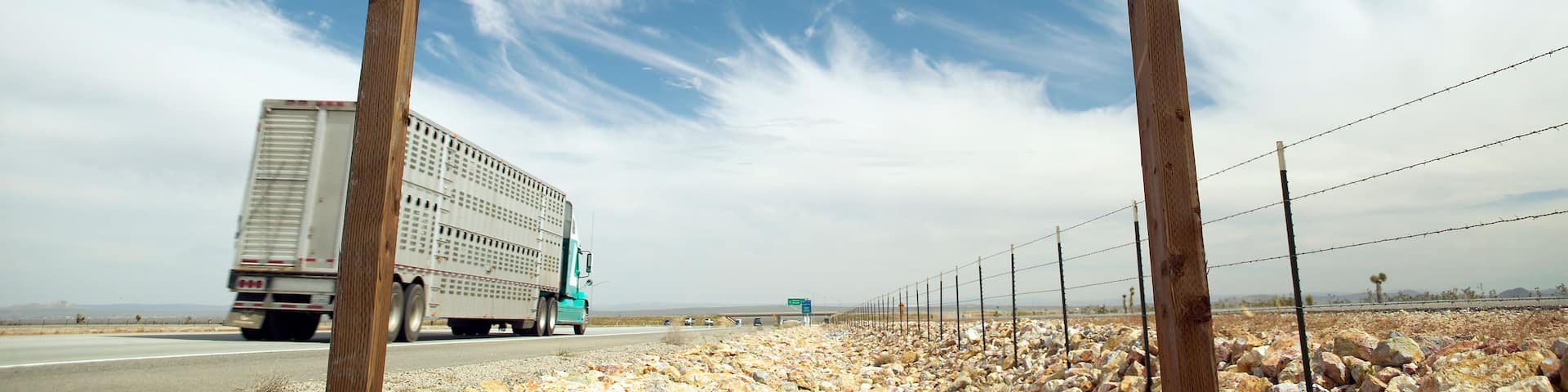 A green highway exit sign for California City with a clear sky and a truck on the road.