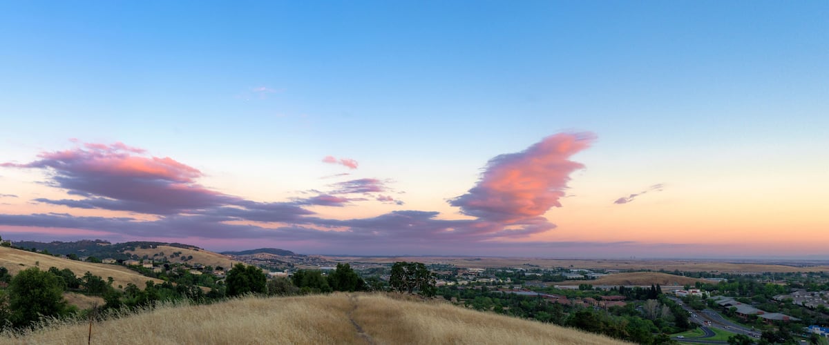 A sunset over a valley with rolling hills and a town in the distance.