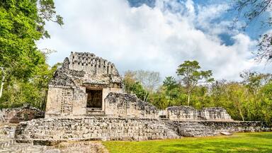 An ancient stone structure with a central doorway, surrounded by lush greenery and a partly cloudy sky.