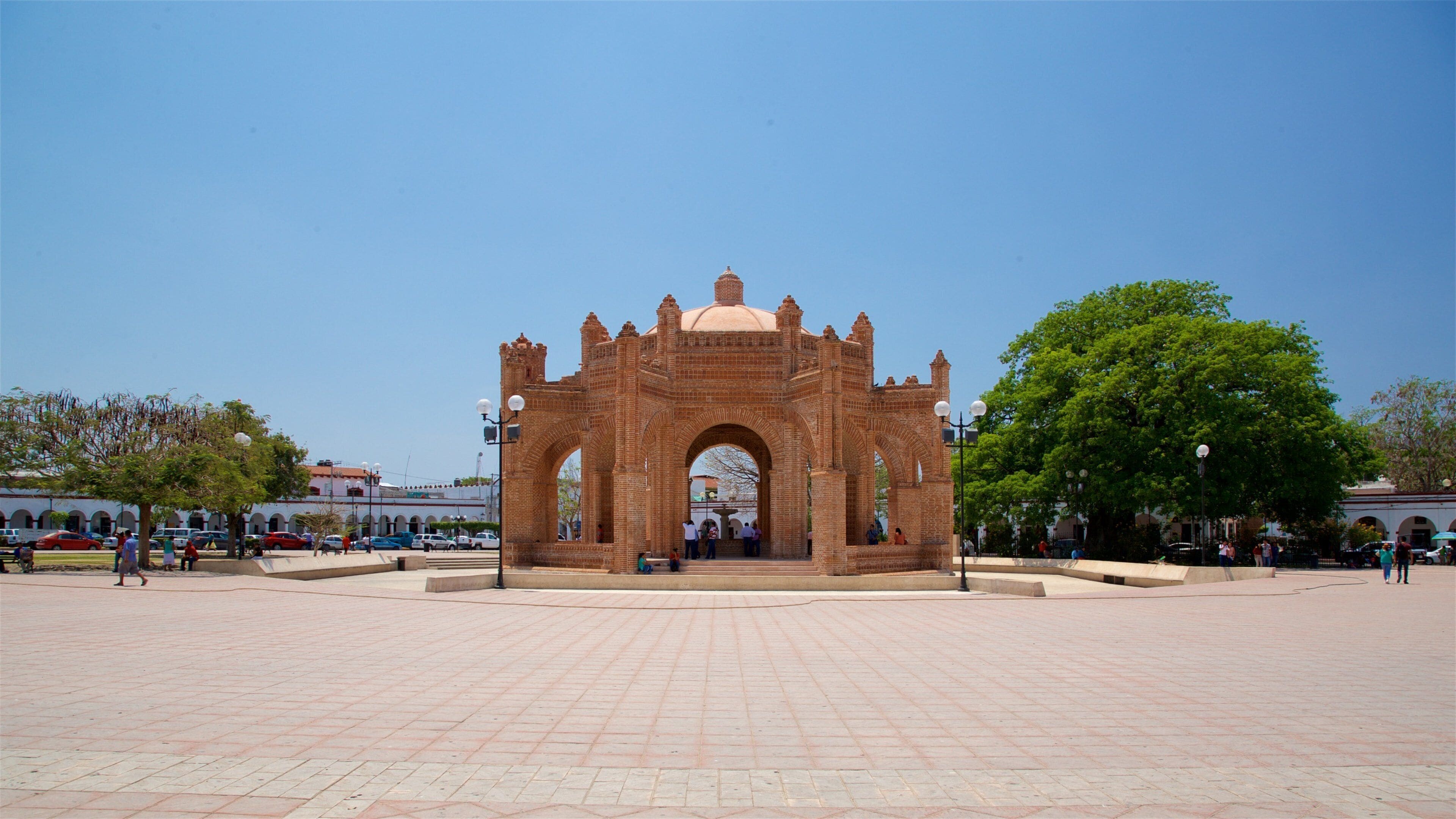 A large brick archway with a dome, surrounded by a paved plaza with trees and people.