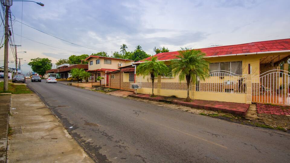 A residential street with houses, palm trees, and a red-roofed building.
