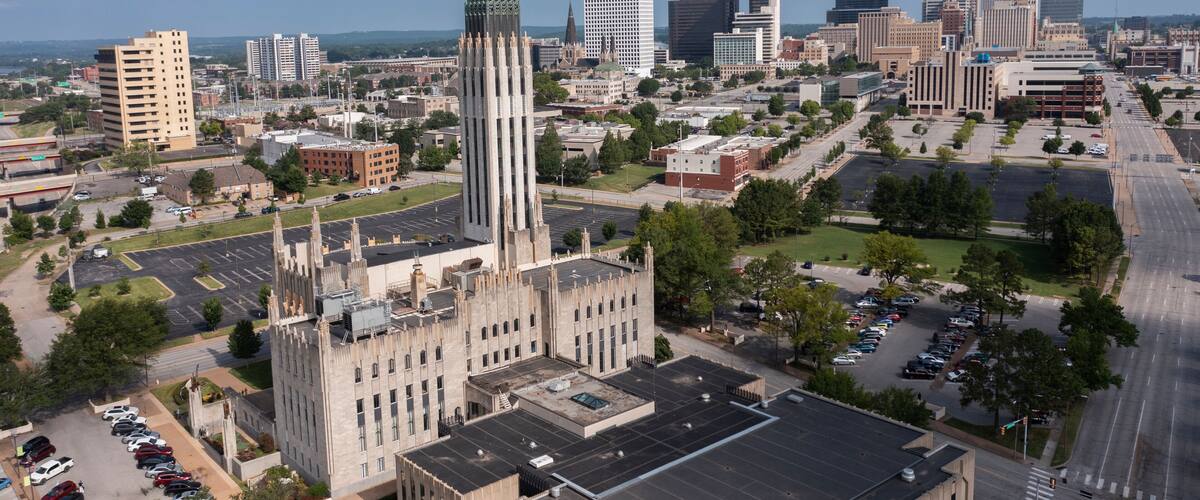 A cityscape with a prominent historic building featuring a tall spire, surrounded by modern high-rise buildings and a mix of urban and green spaces.