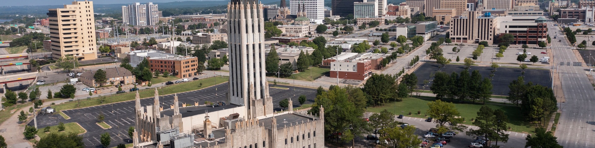 A cityscape with a prominent historic building featuring a tall spire, surrounded by modern high-rise buildings and a mix of urban and green spaces.