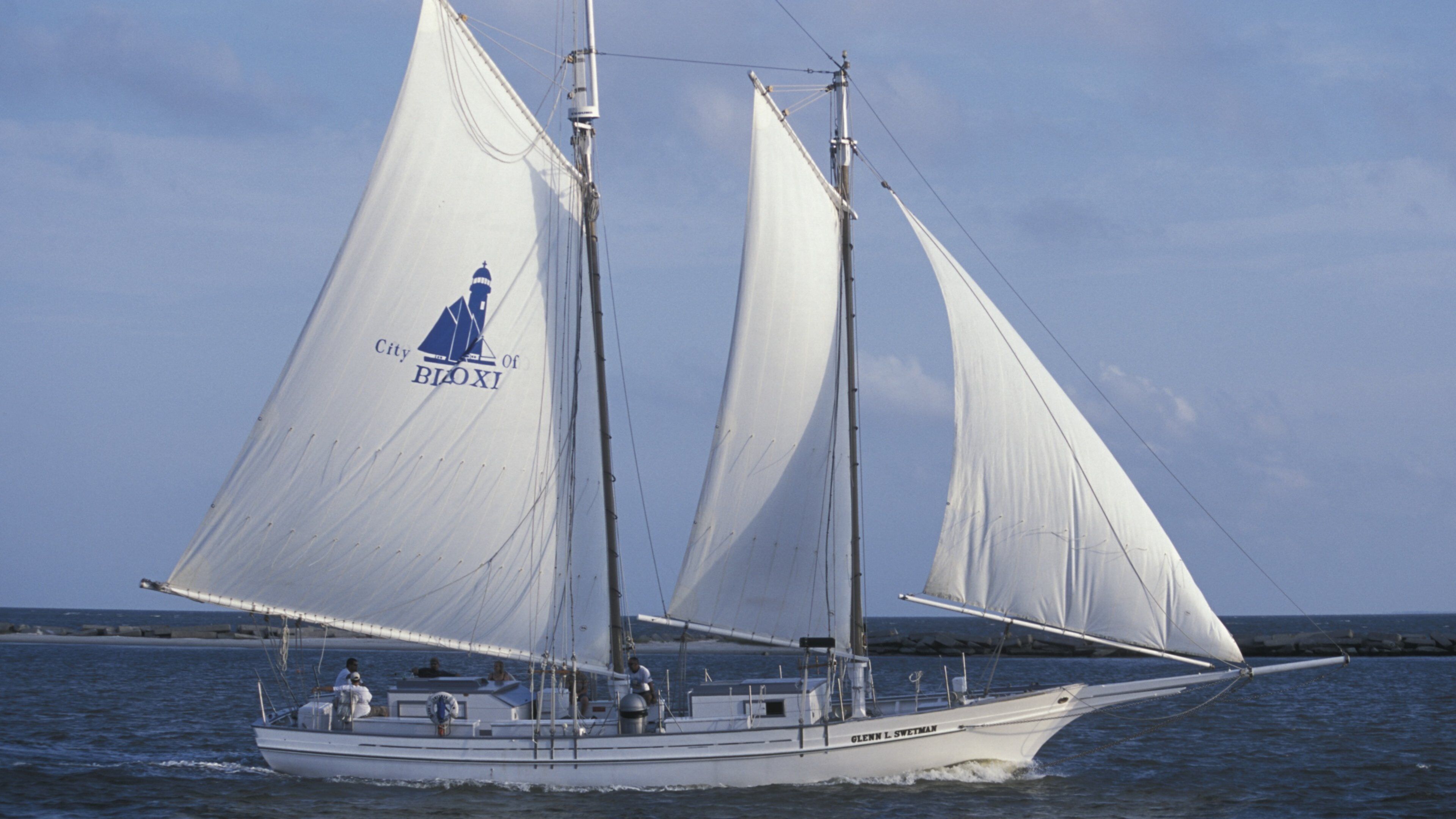 A sailboat with white sails and a logo on the sail, sailing on the water.
