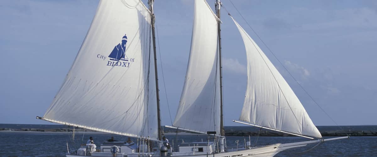 A sailboat with white sails and a logo on the sail, sailing on the water.