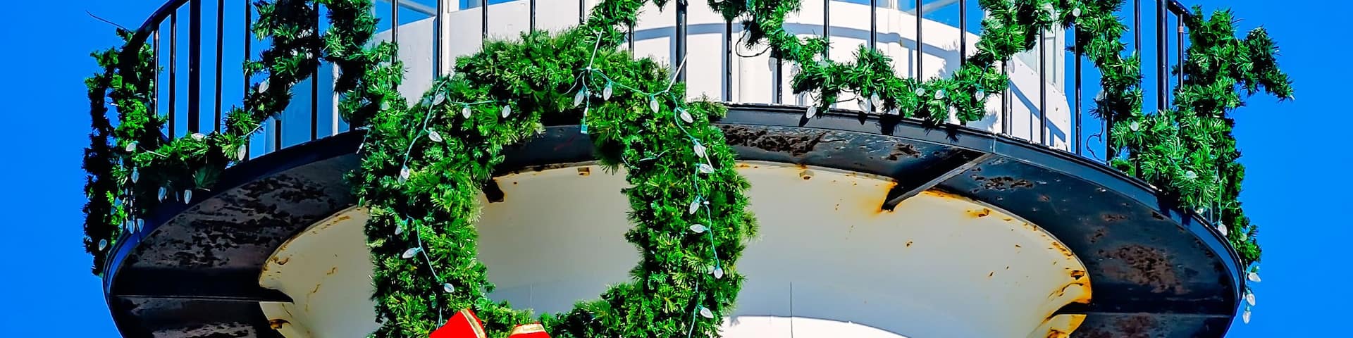 A lighthouse with a white dome, a red bow, and green wreaths.