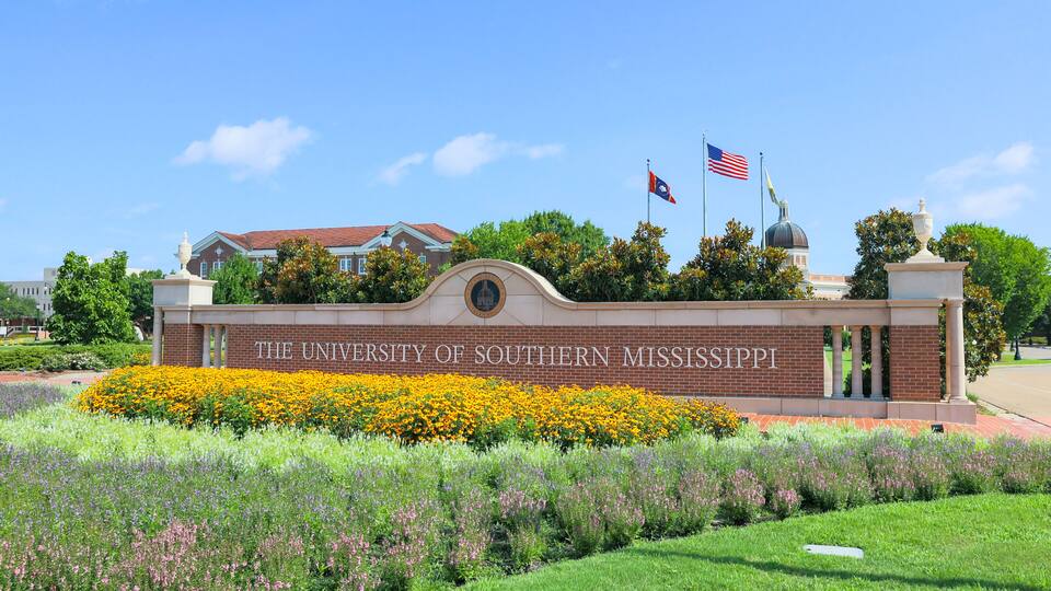 The University of Southern Mississippi's entrance with a brick wall, a dome, and two flags.
