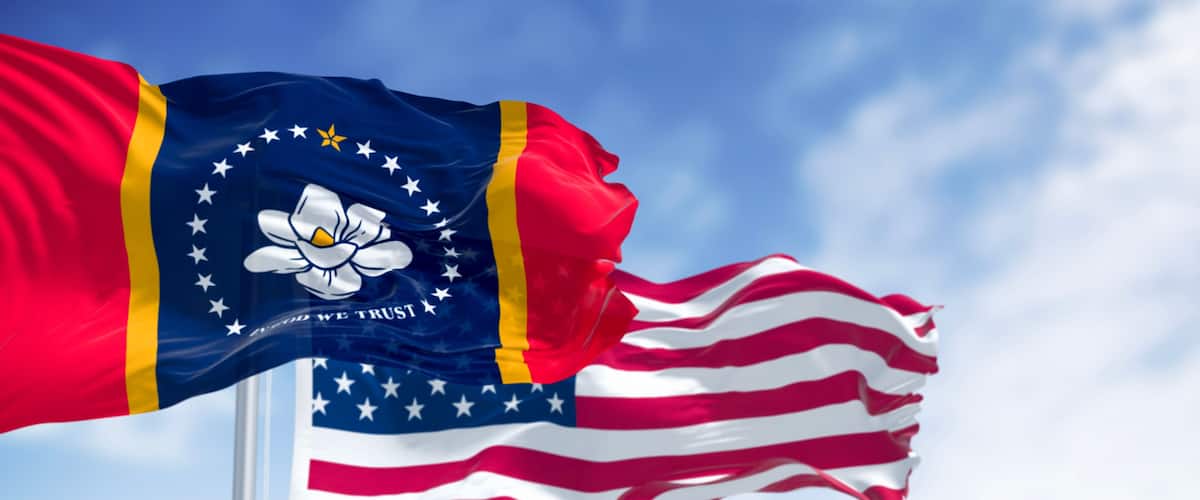 A flag with a blue field, white stars, and a white flower emblem, alongside a red and white striped flag.