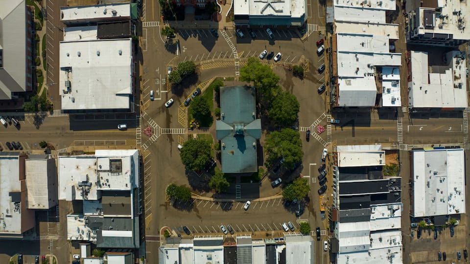 An aerial view of a city intersection with multiple buildings, roads, and parked cars.