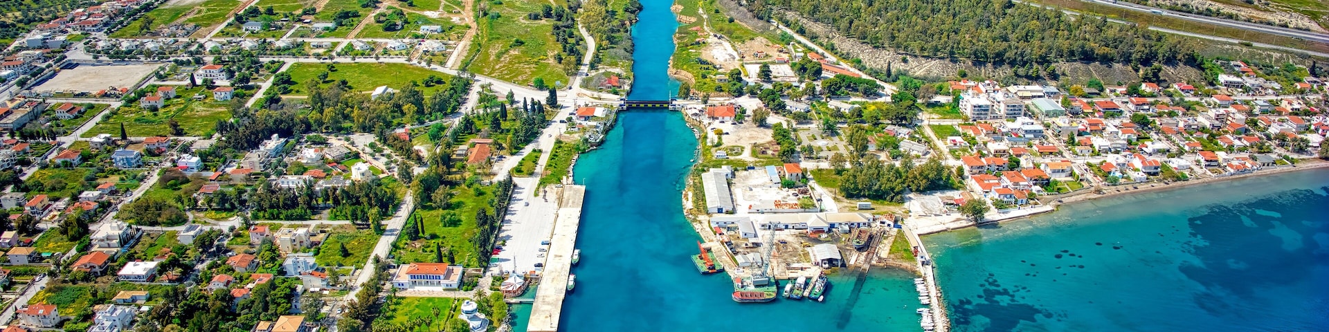 Vista aérea de uma cidade costeira com uma ponte imponente, águas turquesa cristalinas e um porto de iates.