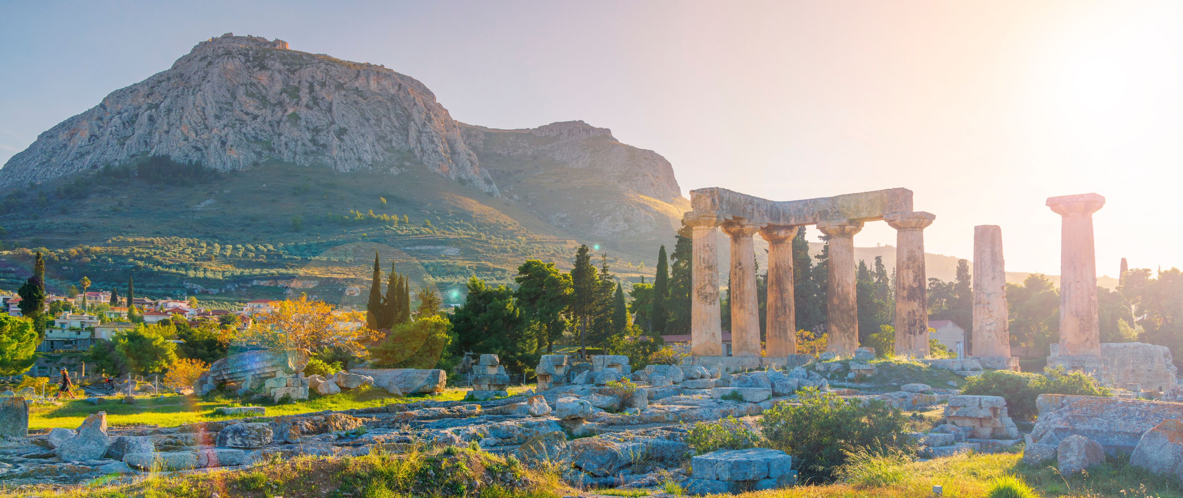 Ancient ruins with columns, a mountain, and a town in the background.