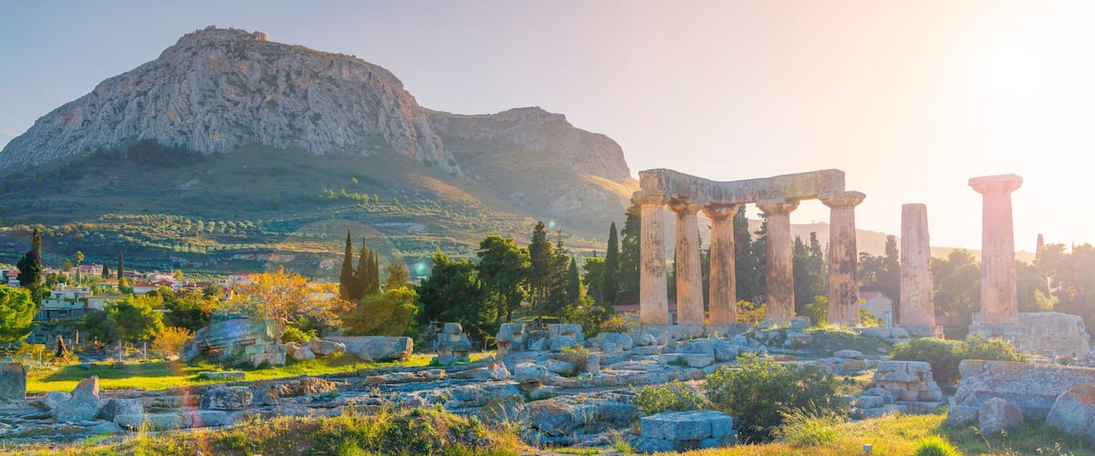 Ancient ruins with columns, a mountain, and a town in the background.
