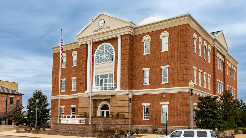 A large brick building with a clock tower and a flagpole with the American flag.