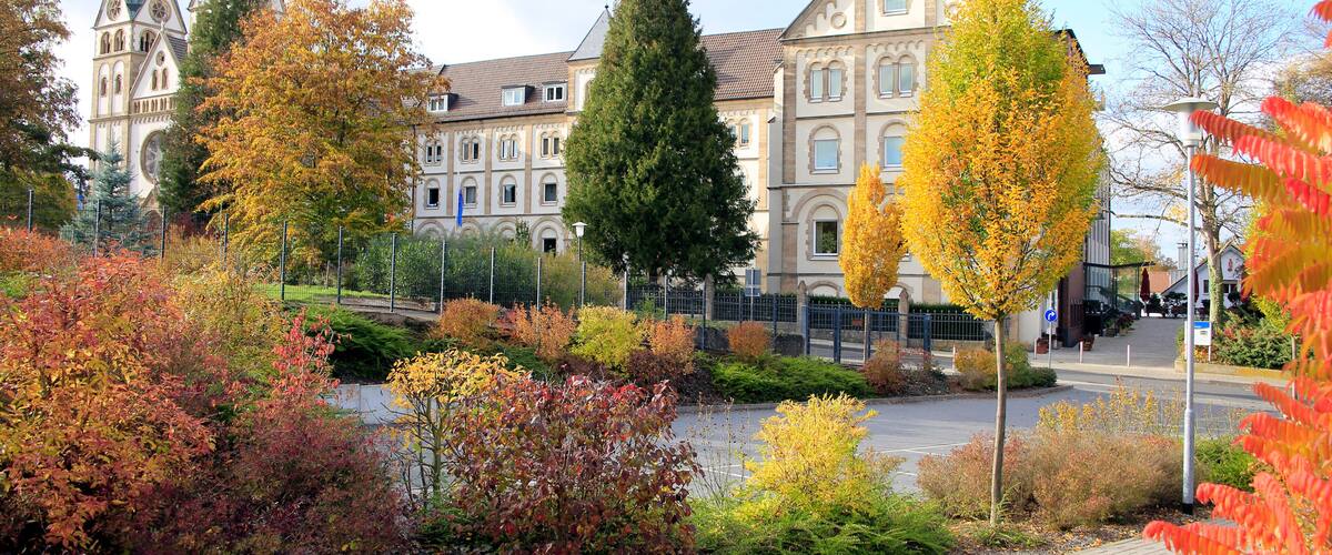 A historic building with towers, surrounded by autumn foliage and a paved walkway.