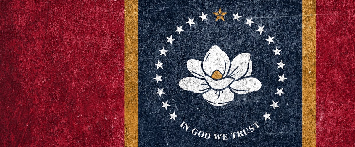 A flag with a white flower emblem, stars, and the phrase 'IN GOD WE TRUST' on a red background.