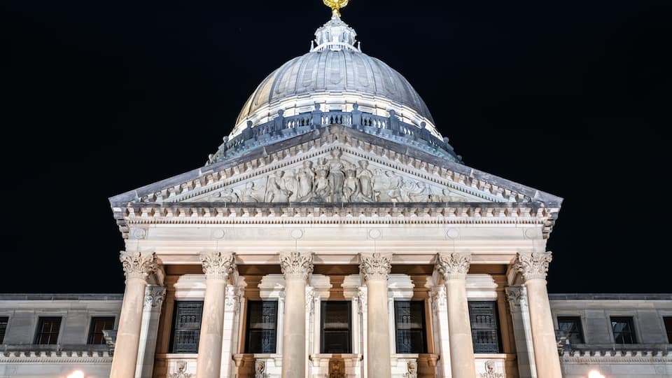 A grand neoclassical building with a large dome and golden eagle atop, illuminated at night.
