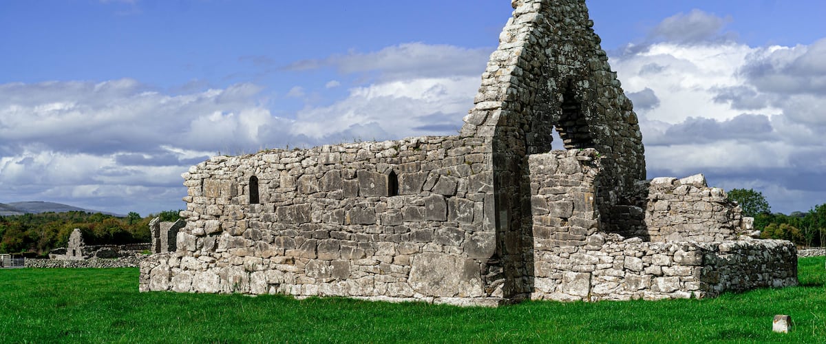 An ancient stone ruin with a tall, narrow tower, set against a backdrop of a clear blue sky and green grass.