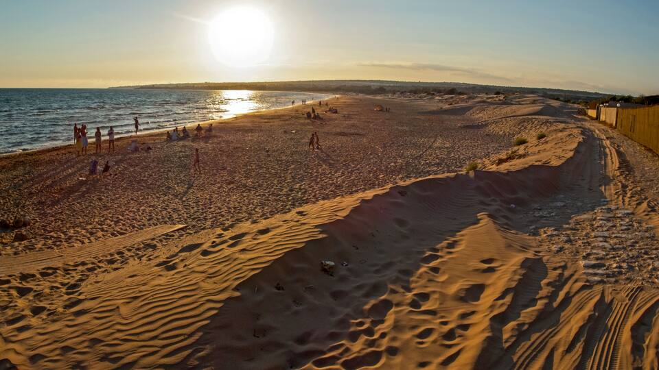 A beach with sand dunes, a clear sky, and the ocean.