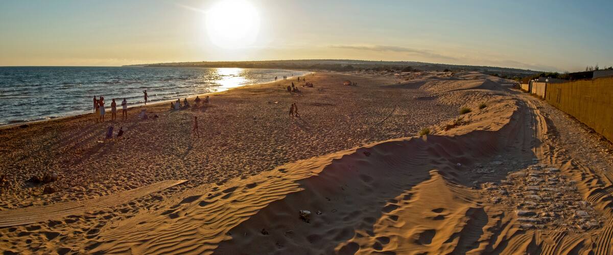 A beach with sand dunes, a clear sky, and the ocean.