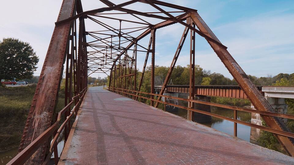 A rusted metal bridge with a brick walkway over a river.
