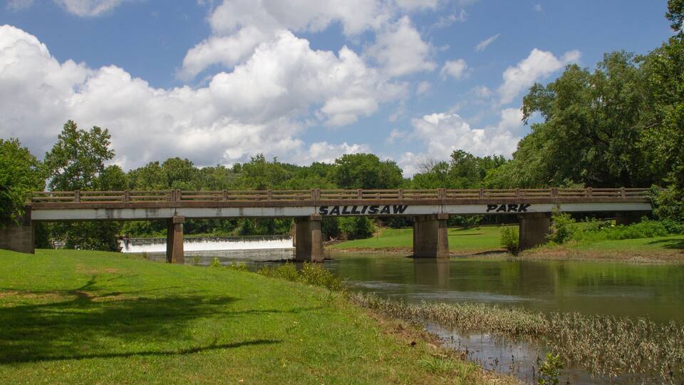 A bridge labeled 'Sallisaw Park' over a river with grassy banks and trees in the background.