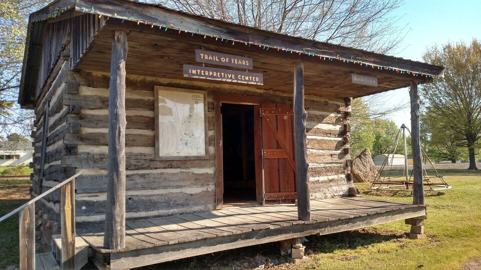A rustic wooden cabin labeled 'Trail of Tears Interpretive Center' with a porch and a swing set in the background.