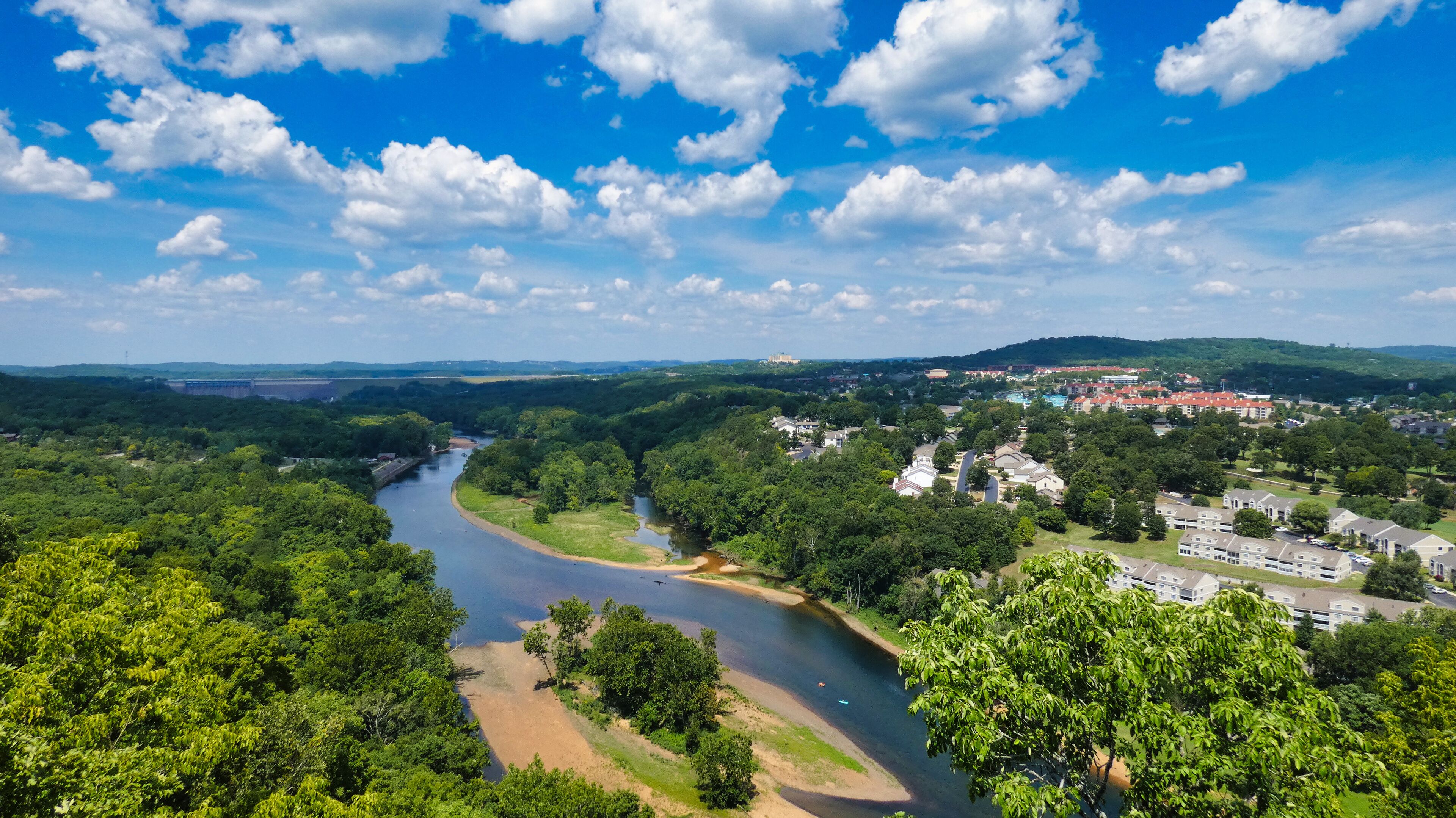 A river winding through a forested area with a town in the background.