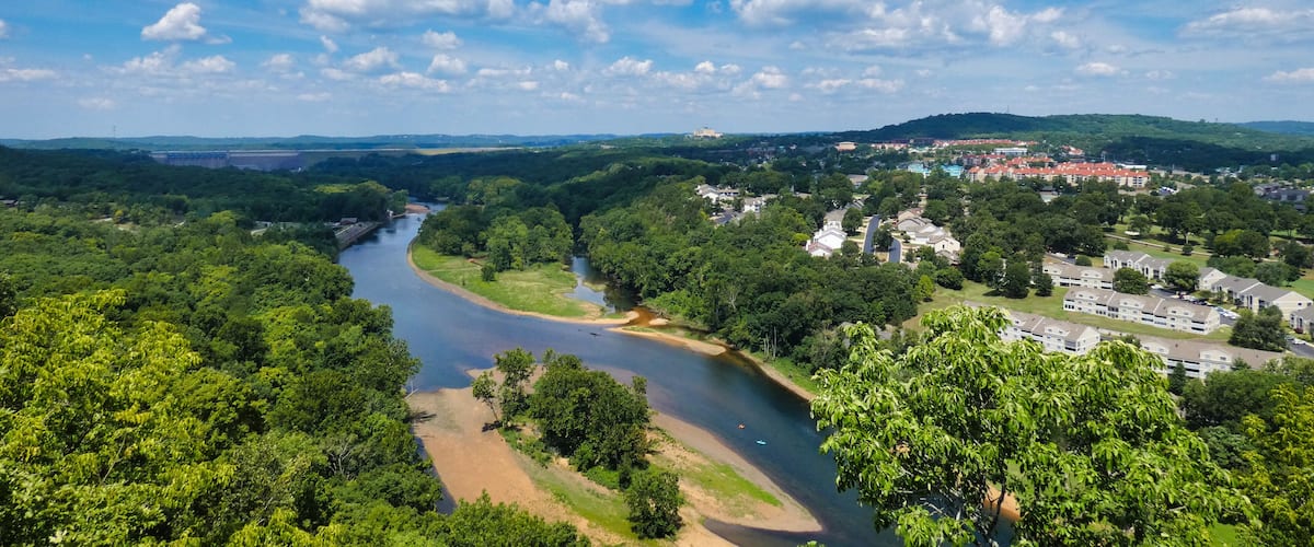 A river winding through a forested area with a town in the background.