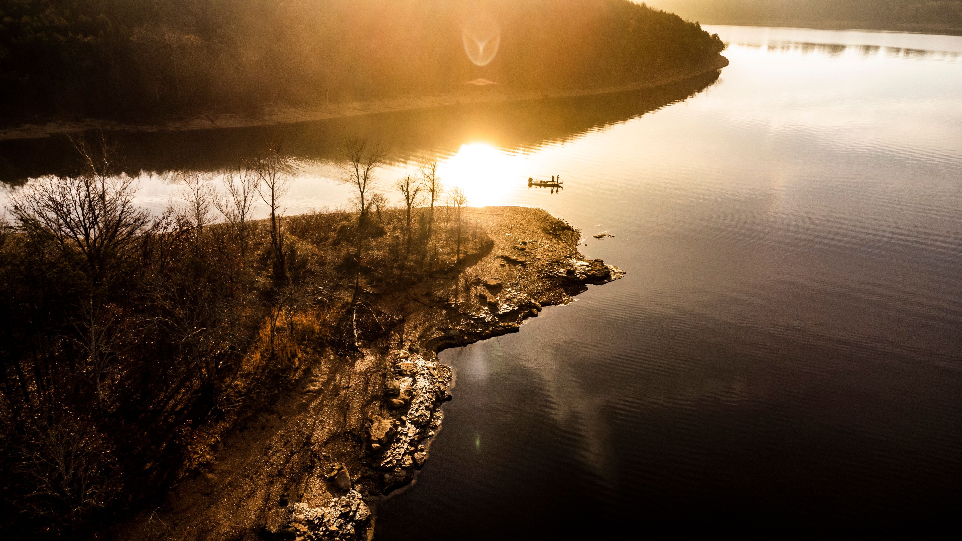 A calm lake with a rocky shoreline, trees, and a boat.