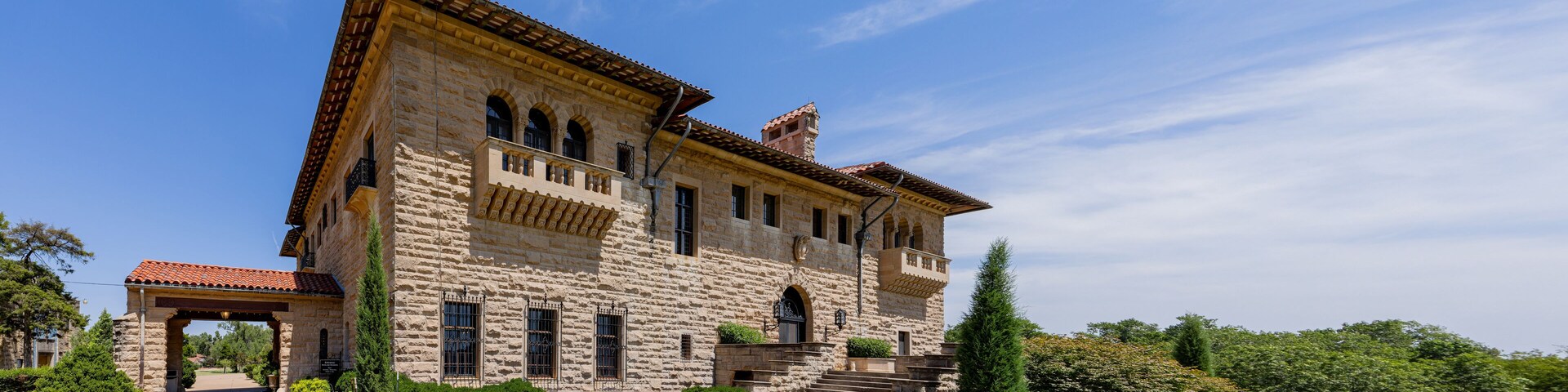 A large stone building with a red-tiled roof, arched windows, and a staircase leading to the entrance.