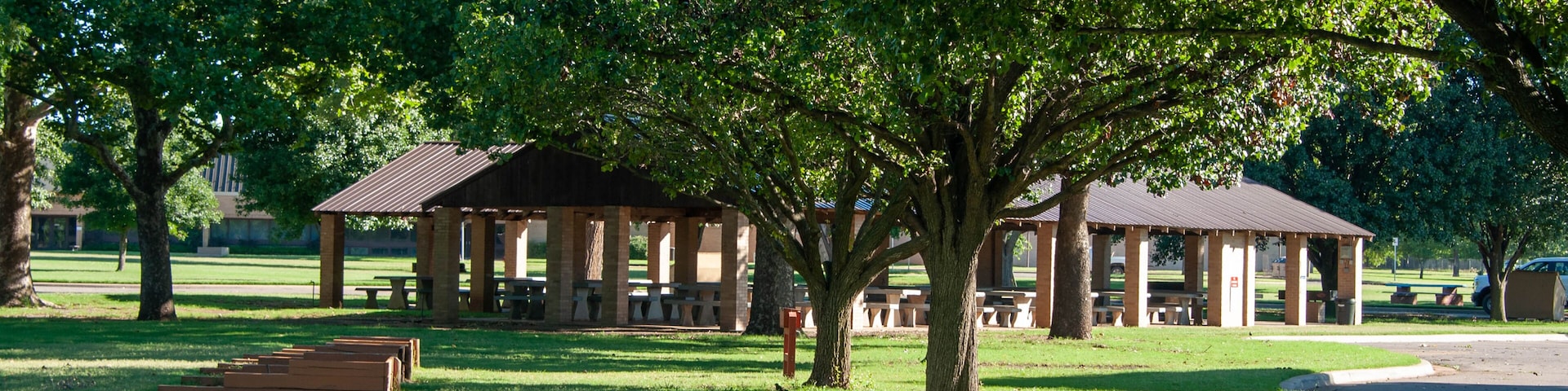 A park with picnic shelters, a large tree, and a grassy field.