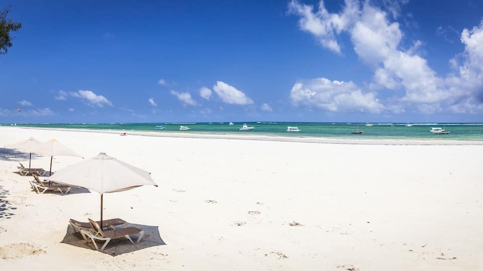 A beach with white sand, clear turquoise water, and several boats in the distance.