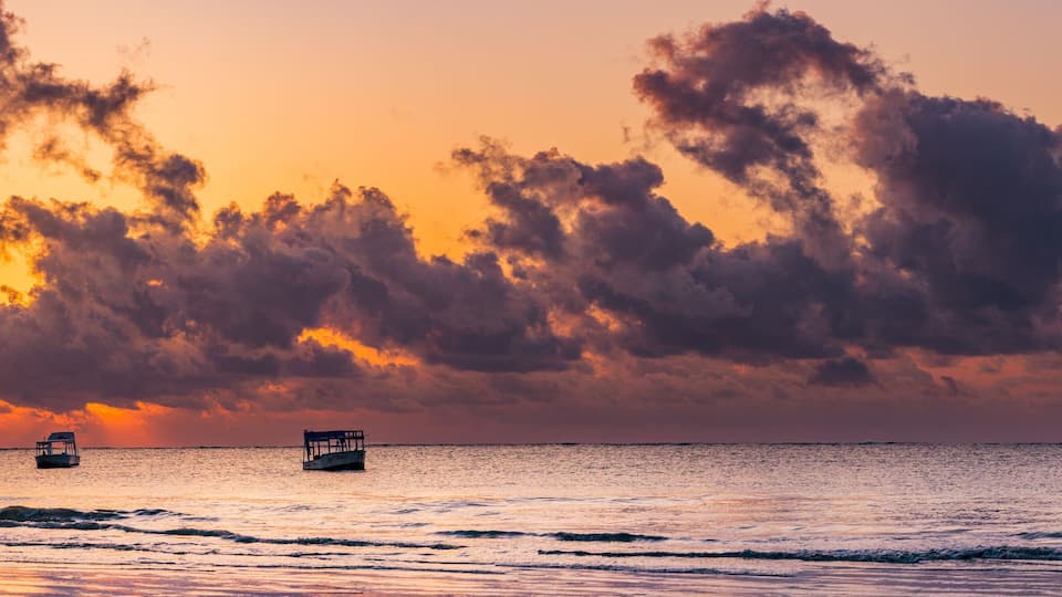 A sunset over the ocean with two boats.