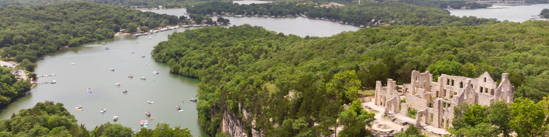 A river surrounded by dense forest, a historic stone building, and a distant bridge.