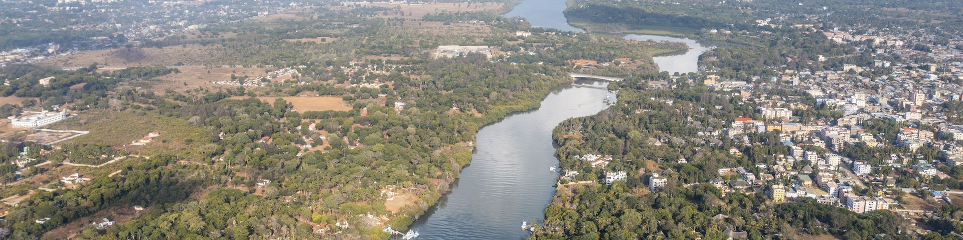 Aerial view of Mtwapa Creek winding through verdant trees, with boats dotting the dark water, under a bright sky, Mombasa, Mombasa County, Kenya.
