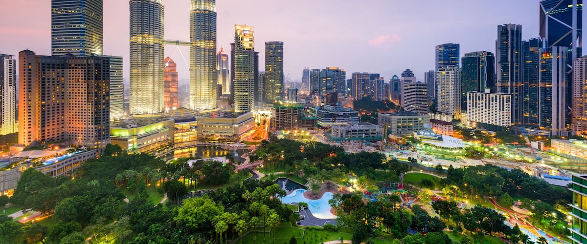 A cityscape with prominent skyscrapers, including the Petronas Towers, and a well-maintained park area.