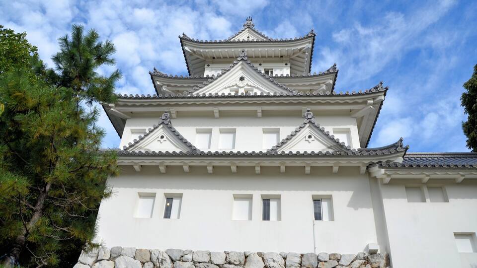 A traditional Japanese castle with multiple tiers, white walls, and a stone base.