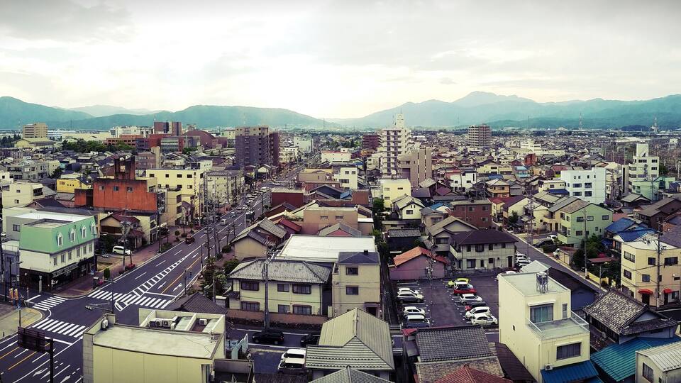 A cityscape with a mix of traditional and modern buildings, a wide road, and mountains in the background.