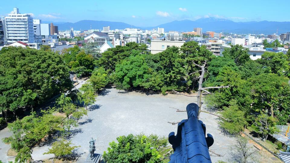 A cityscape with a park area, trees, and a statue.