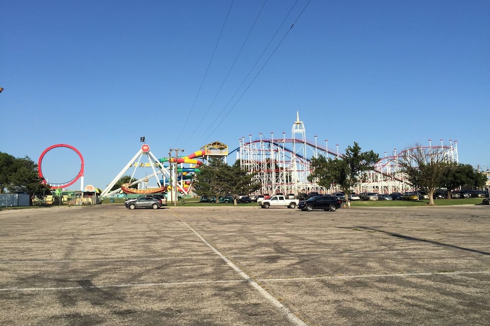 A large parking lot with a roller coaster, a Ferris wheel, and a water slide.