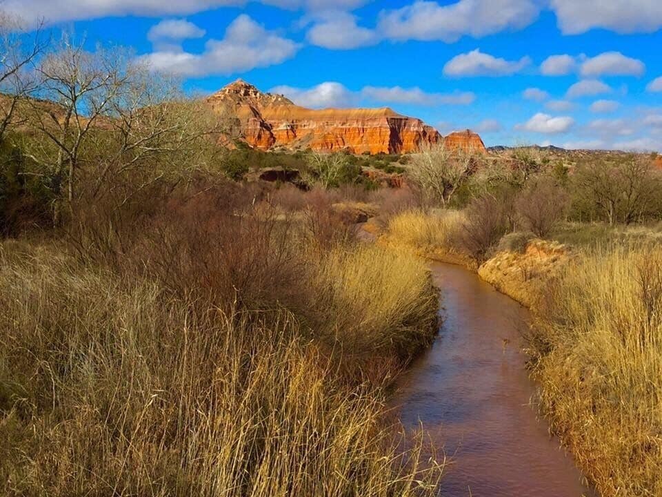 Un lecho de río seco con vegetación escasa y una montaña rocosa al fondo.