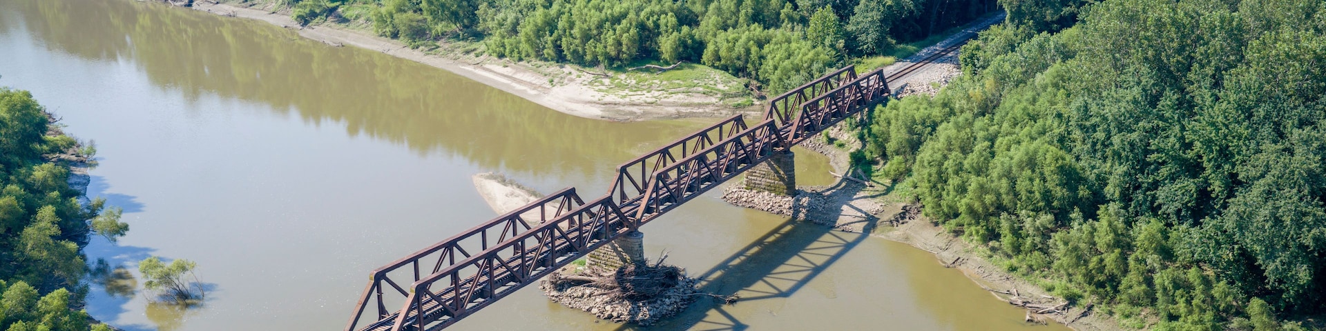 A steel bridge spanning a river, surrounded by dense forest.