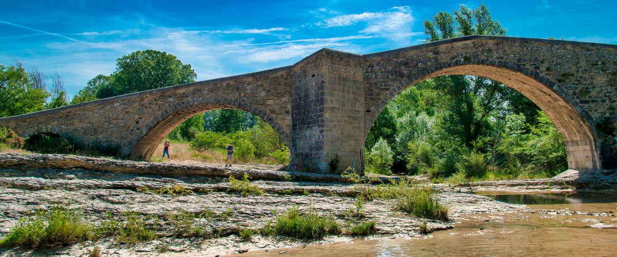 An ancient stone bridge with three arches over a river, surrounded by lush greenery and trees.