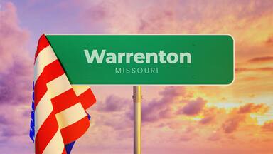 Uma placa de rua verde com a inscrição 'Warrenton Missouri', ao pôr do sol.