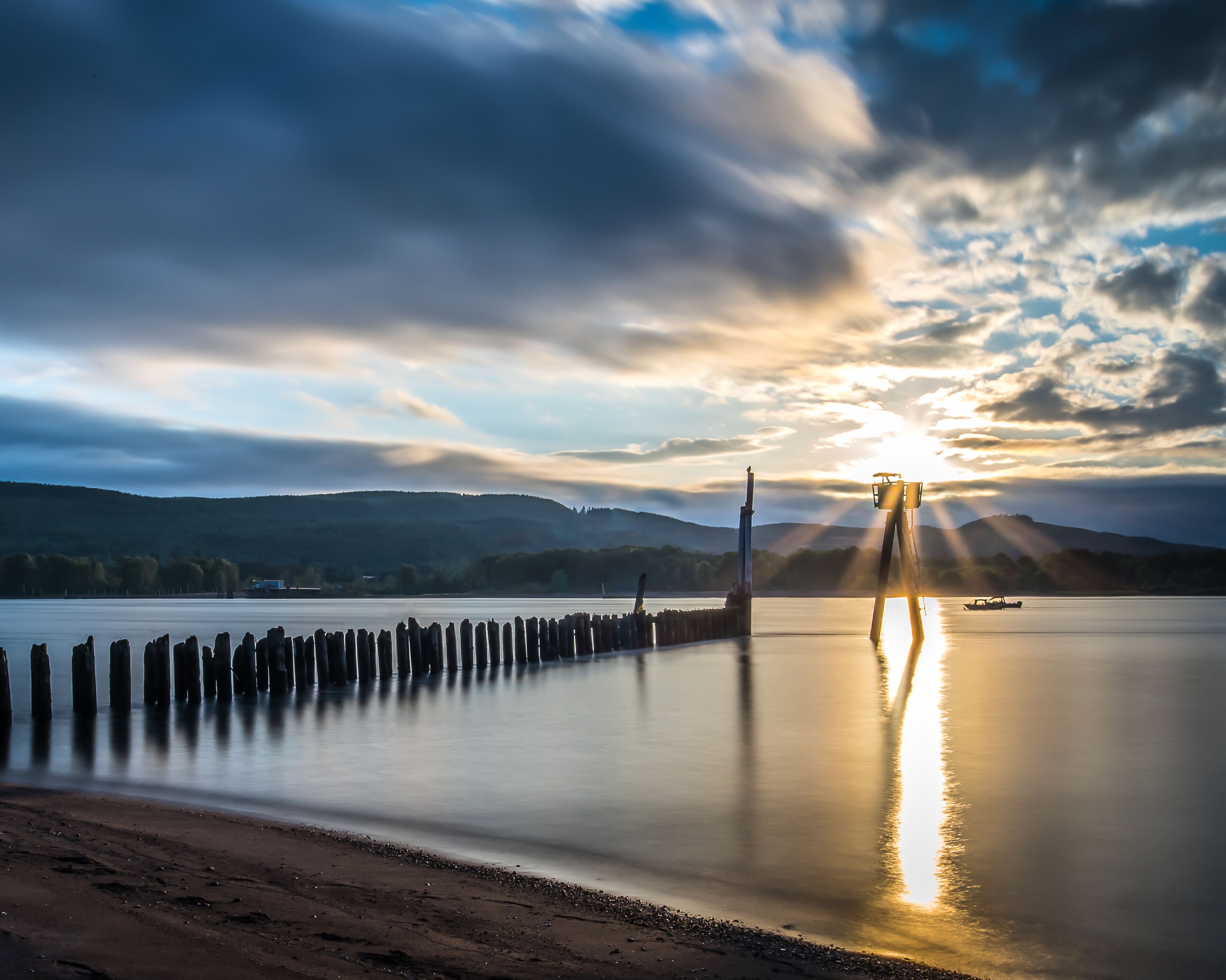 A calm lake with a wooden pier, a lighthouse, and a sunset.